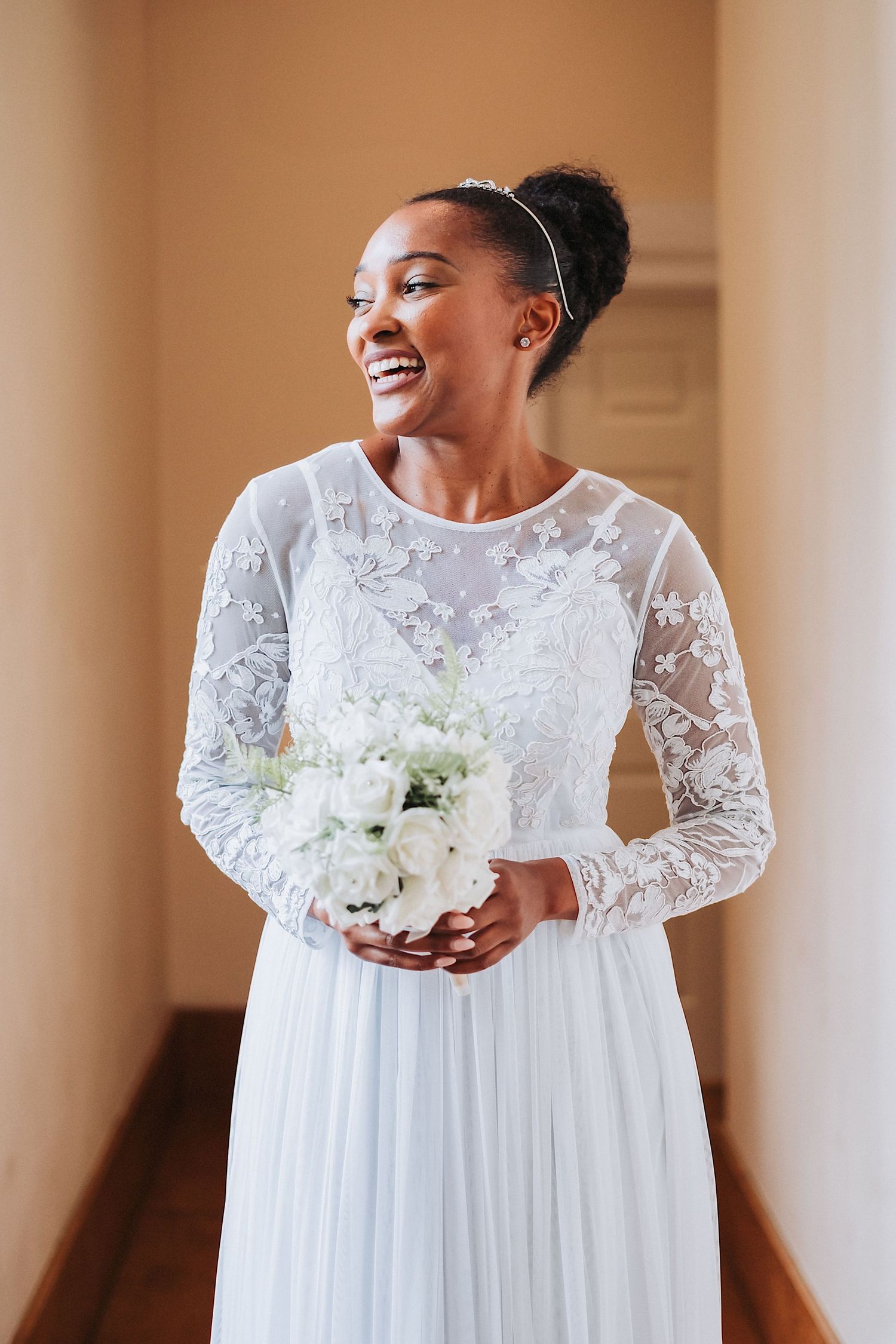 A radiant bride in lace gown holds elegant white and green bouquet during outdoor portrait session.