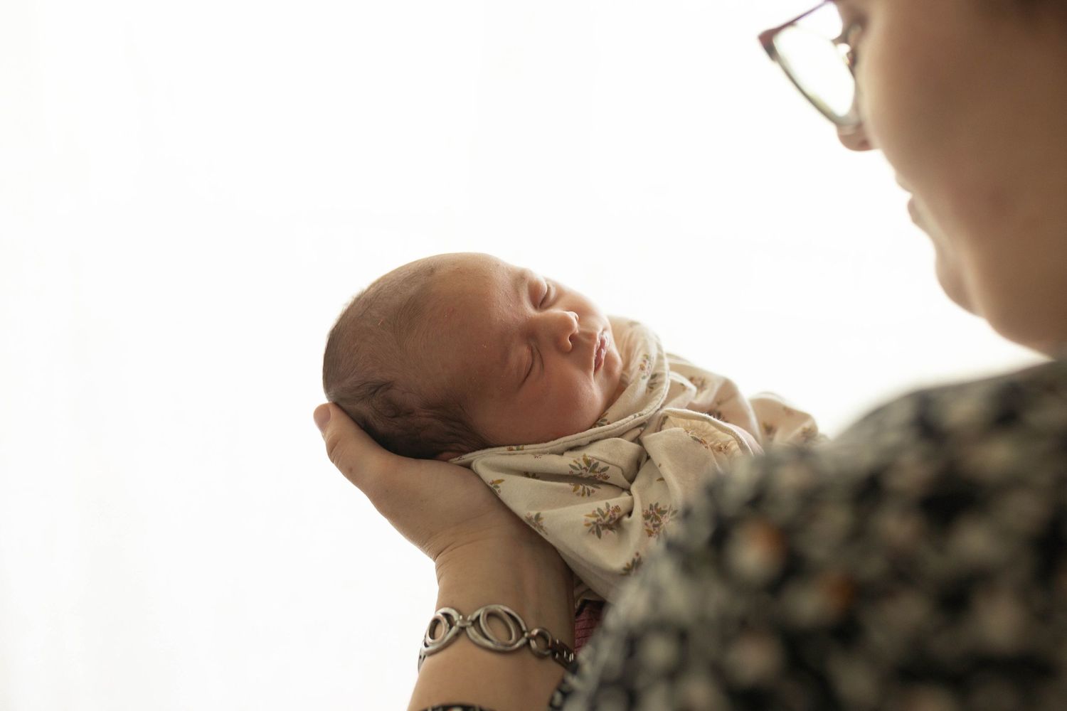 Nouveau-né endormi paisiblement dans les bras de ses parents sur fond blanc, pureté et douceur en studio photo à Niort.