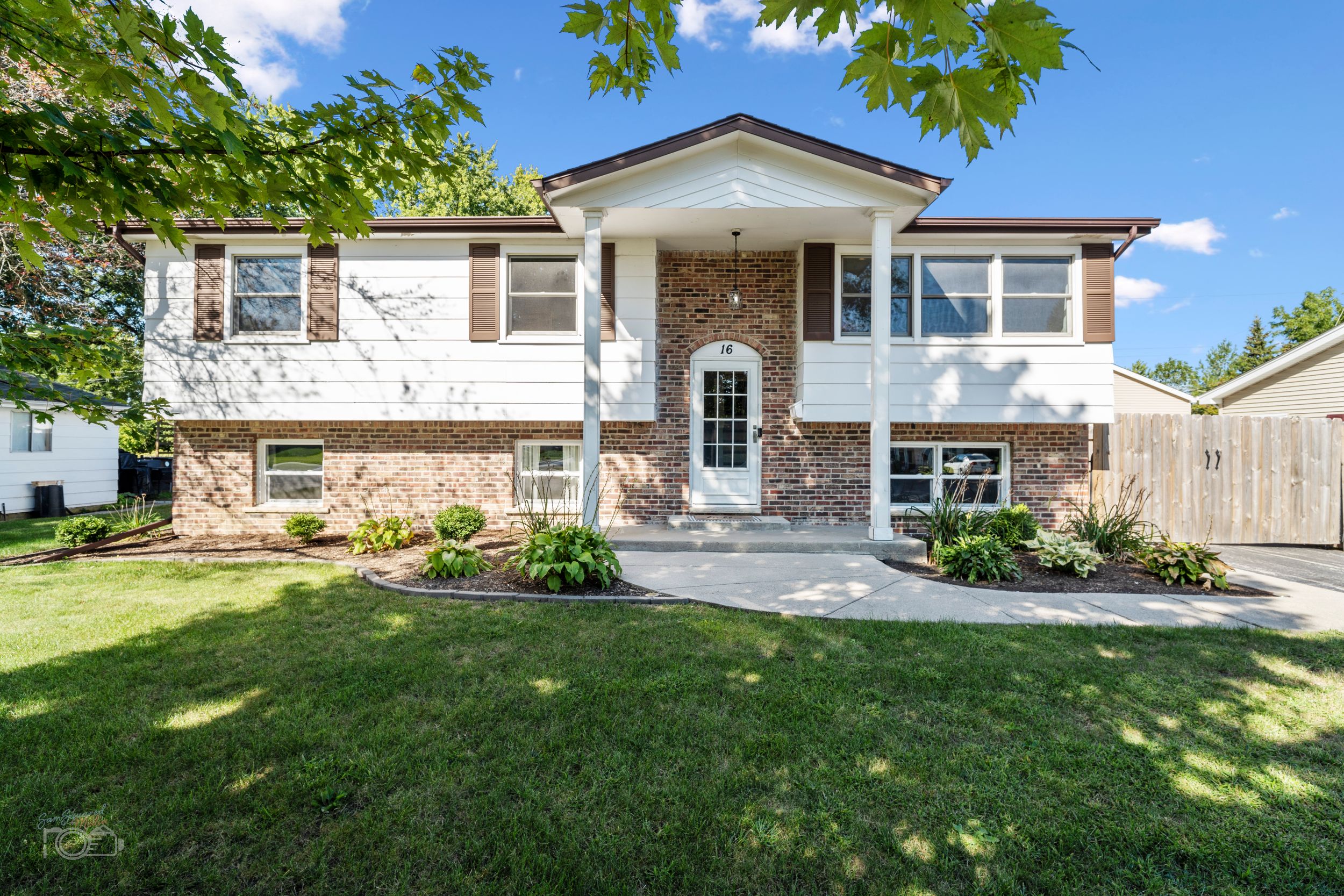 Split-level home with stone veneer facade, white siding, and well-maintained front lawn on a sunny day.