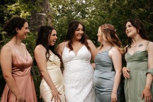 A bridal party in different colored pastel dresses stands together outdoors smiling in a garden setting. Photo at Montague PEI