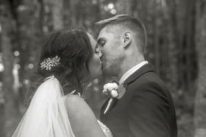 A romantic black and white wedding photo of a couple sharing a kiss in a forest setting. Photo at Clinton Hills