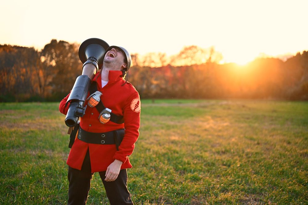 Person in red military costume with a cannon prop posing at golden hour in an open field.