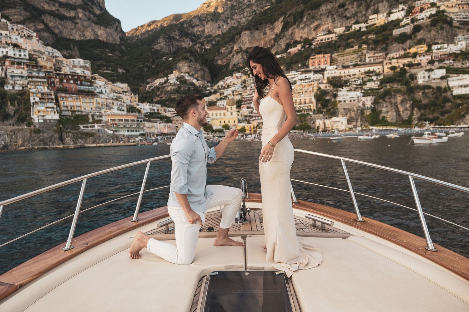A romantic beach proposal scene with Positano's distinctive coastline in the background.