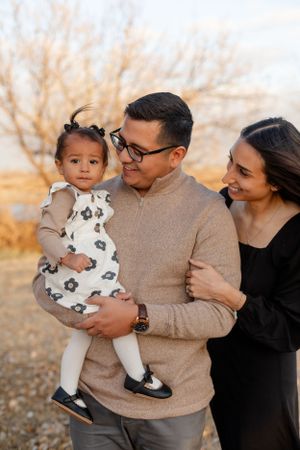 A family poses together outdoors during golden hour wearing coordinated neutral colors.