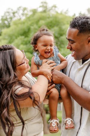 A joyful family moment captured outdoors as parents play with their laughing toddler.