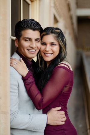 Romantic couple embracing in formal attire against a light architectural backdrop.