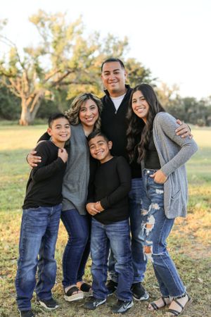 A casual family portrait of five people smiling together outdoors in jeans and sweaters.