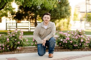 A casual outdoor portrait in a garden with blooming pink roses and brick pathways.