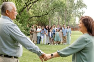 Large family gathering in a park as couple joins hands in the foreground with group watching in background.