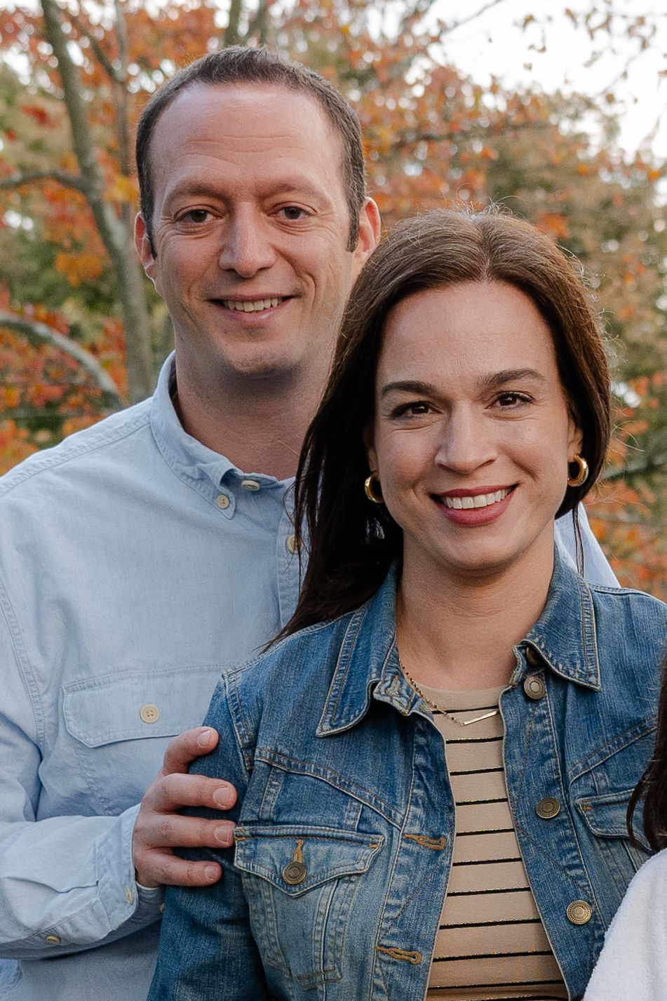 A couple poses outdoors during autumn with fall foliage creating a colorful backdrop.