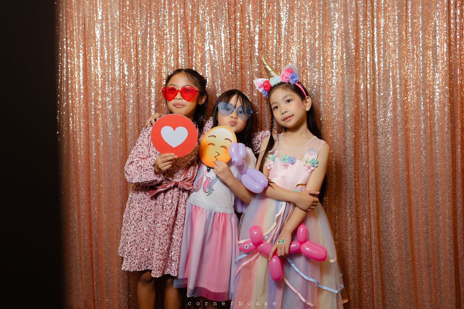 Three people in fancy dresses pose together against a sparkly copper-colored backdrop at a formal event.