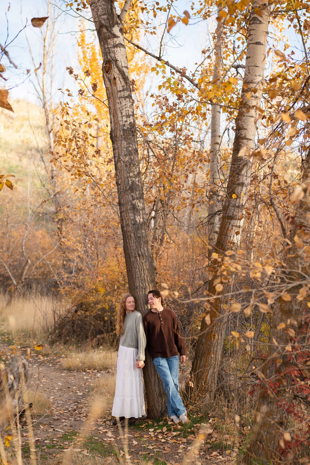 A couple stands among autumn birch trees with golden leaves in a serene woodland setting.