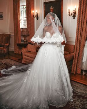 A stunning white wedding gown with lace veil and long train photographed in an elegant room with red curtains and wall sconces.