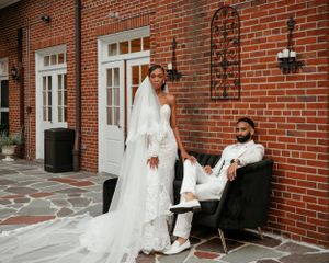 A wedding couple poses in front of a red brick building with white trim and decorative iron wall art.