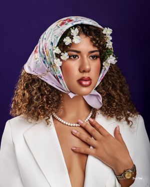 Elegant editorial portrait of a woman wearing a floral headscarf and pearl accessories, striking a confident pose.