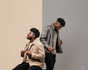 Fashion-forward portrait of a stylish man and woman leaning back-to-back against a neutral background.