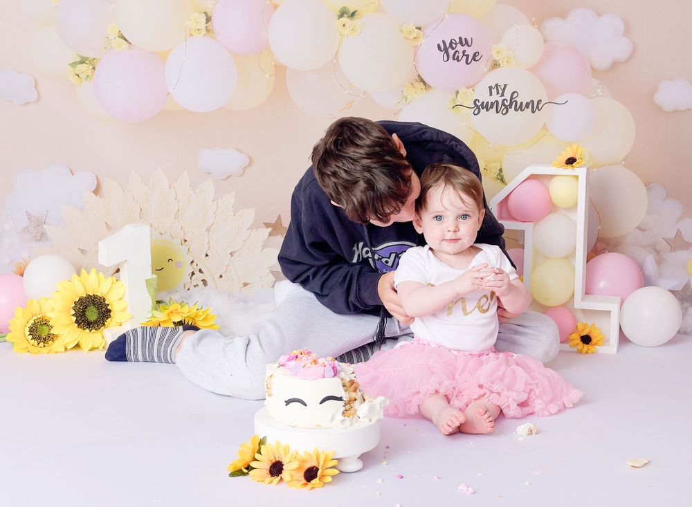 Child sits with her brother at her first birthday cake smash session. Brother cuddles and looks down at his little sister affectionately.