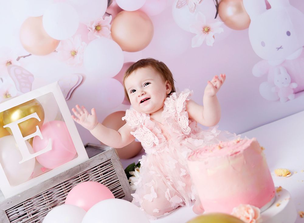 Little girls claps her hands at the cake smash session. Pastel pinks and yummy squidgy cake with lots of balloons and bunnies.