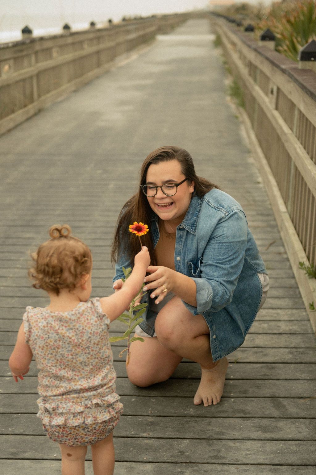 Parent and child share playful moments on a wooden boardwalk at sunset.
