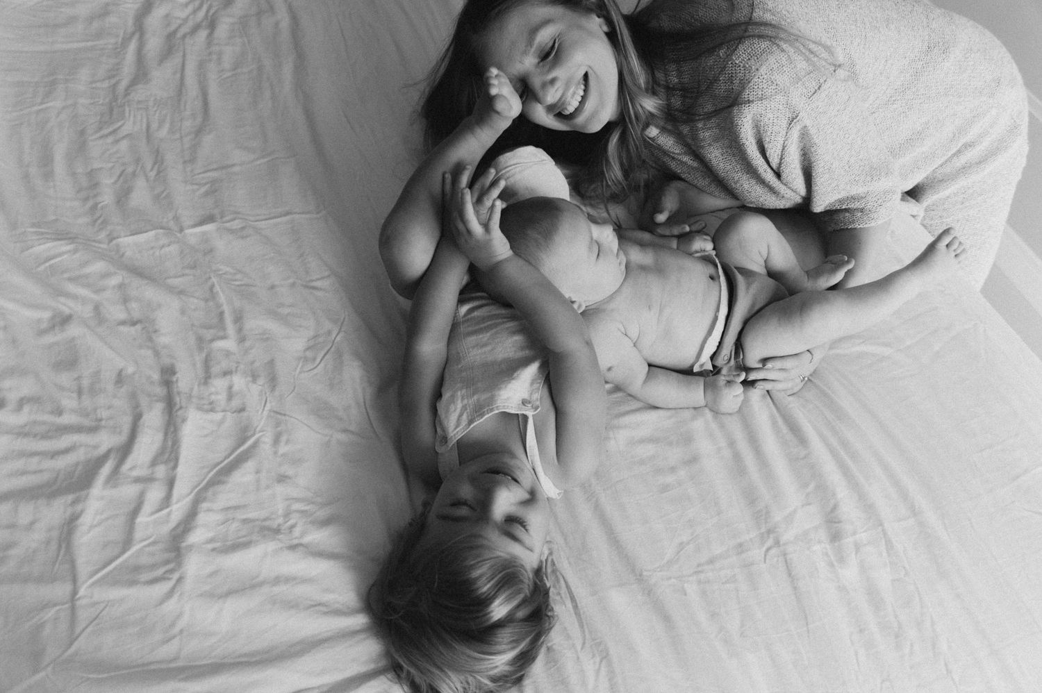 A candid black and white family photo showing joyful laughter while relaxing on a couch with a baby.