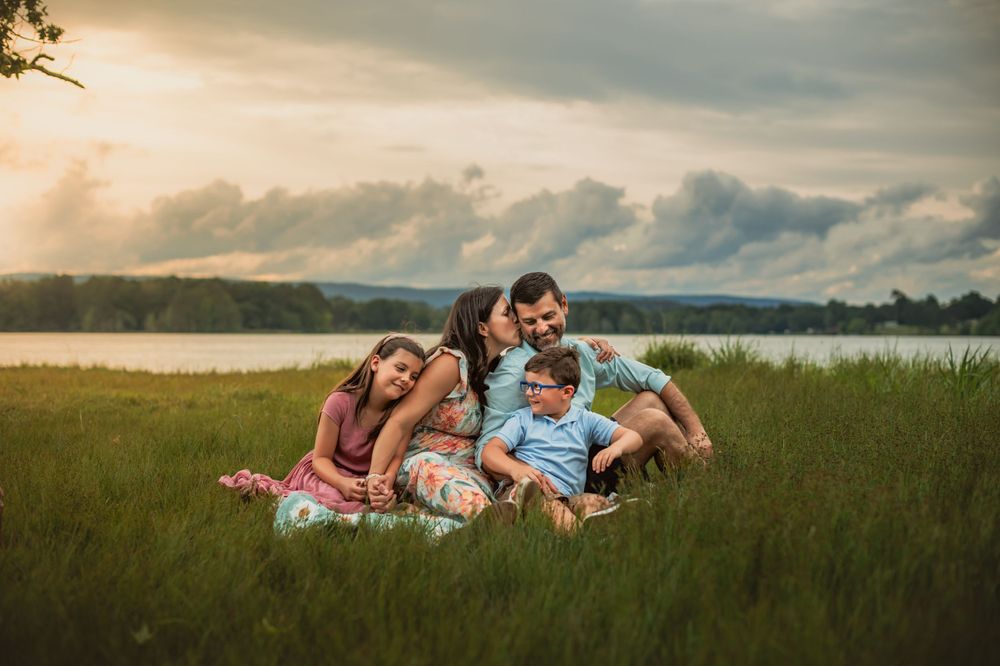 family of 4 cuddles on blanket in tall grass at sunset by lake in Chattanooga