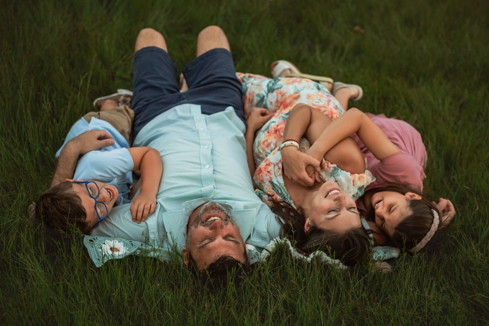 mom and dad snuggle 2 kids on blanket in tall summer grass for family photos in Chattanooga