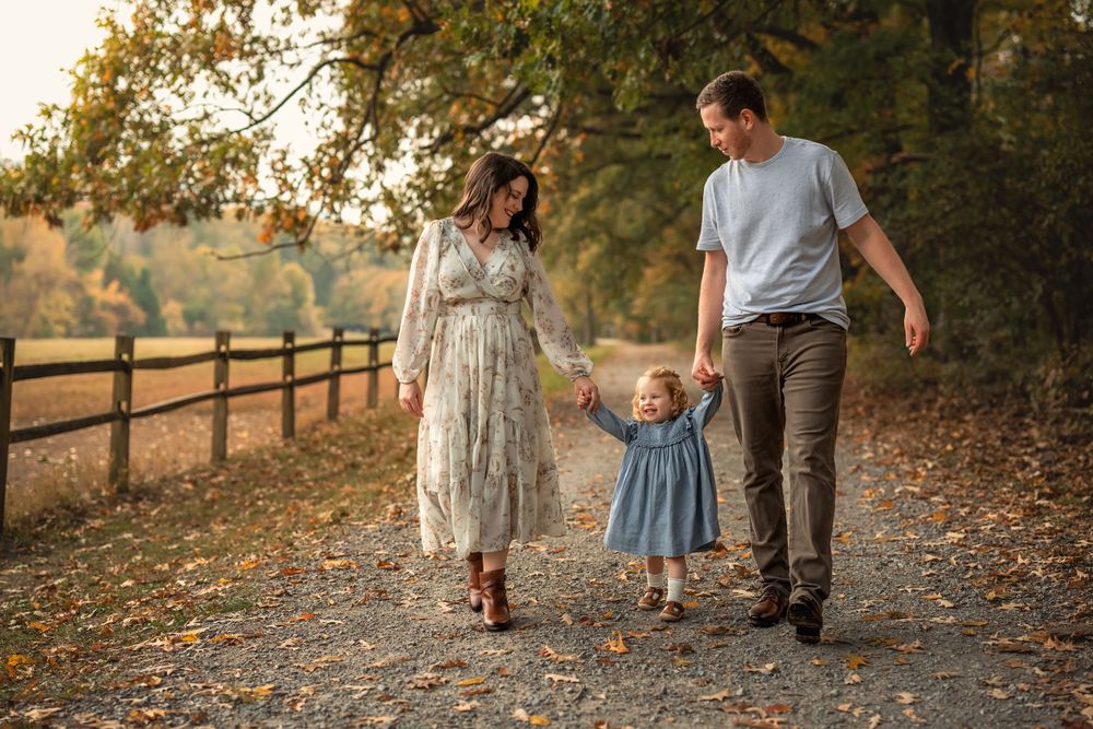 mom and dad hold hands with little girl as they walk a tree-lined path in fall in Chattanooga