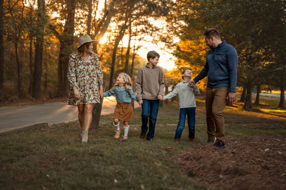 family of 5 holds hands and walks while laughing with each other at sunset