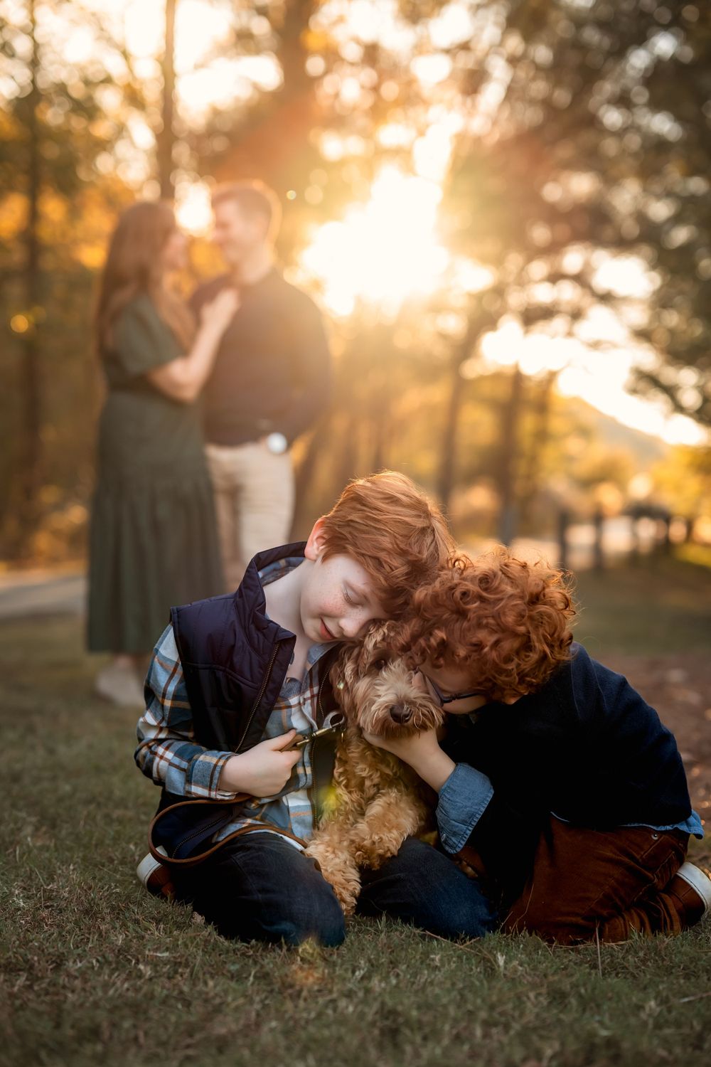 red-head brothers hug their puppy while mom and dad embrace in the background at sunset