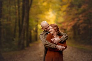 A couple embraces on a forest path surrounded by vibrant autumn foliage and golden sunlight for photo session with Marietta photographer.
