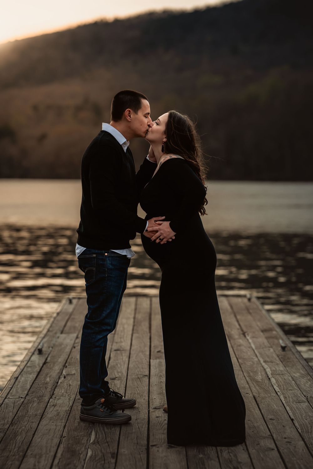husband and pregnant wife kiss on dock at sunset on the Chattanooga river
