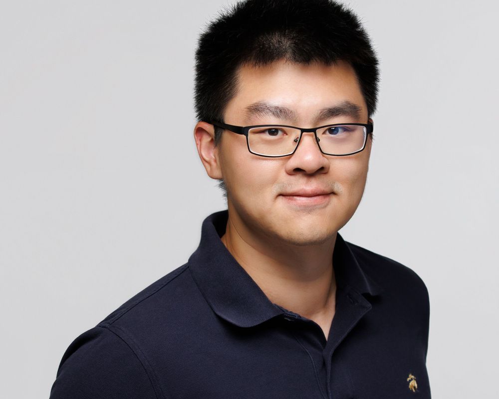 Professional headshot of person wearing navy polo shirt against grey background.