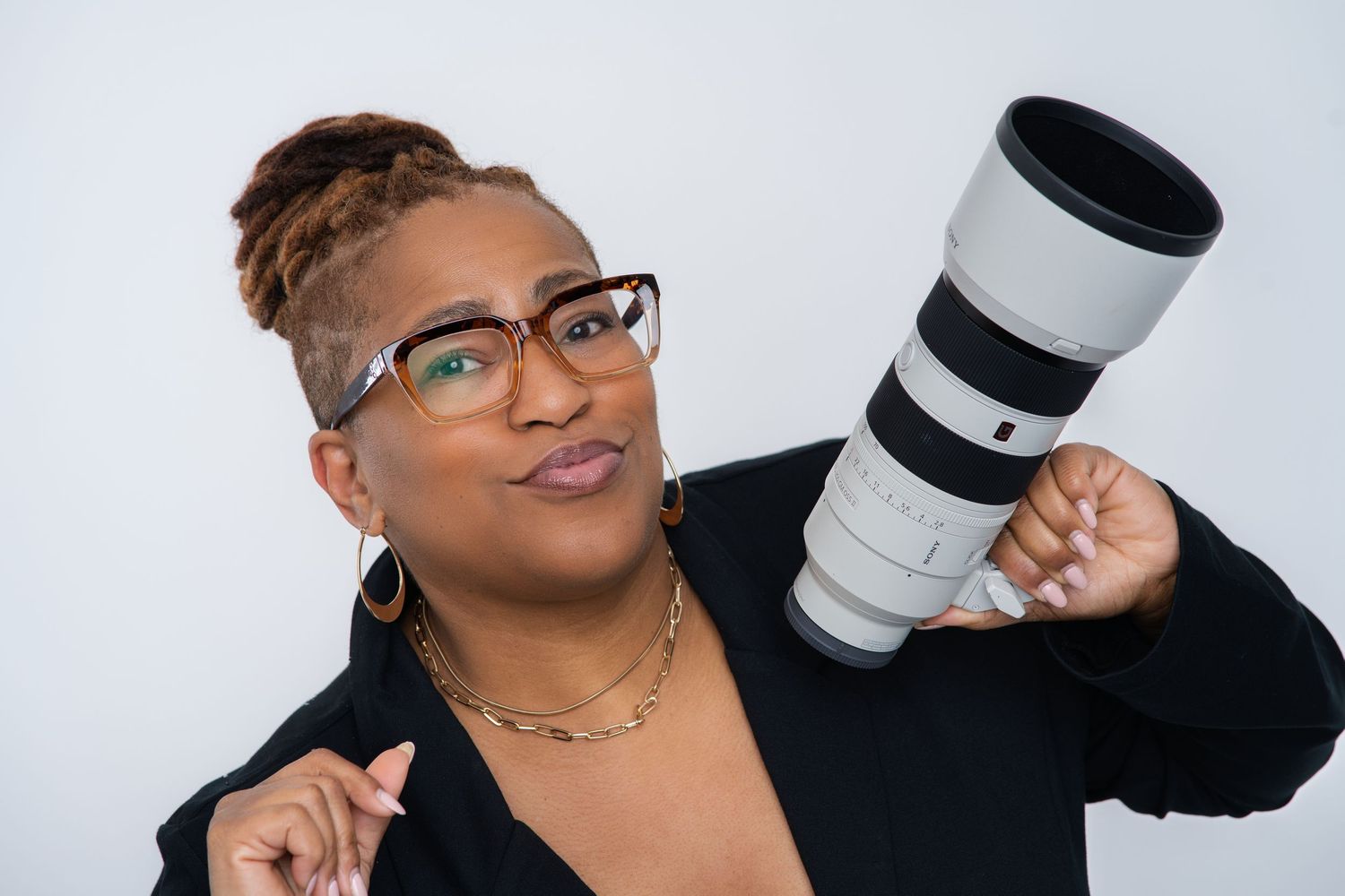 Photographer in black t-shirt holds camera while posing confidently against white backdrop.