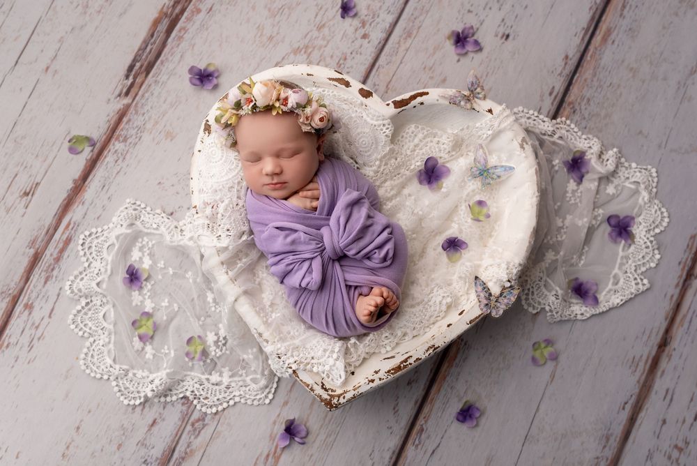 Baby girl in a floral headband sleeping in a heart basket during a newborn session