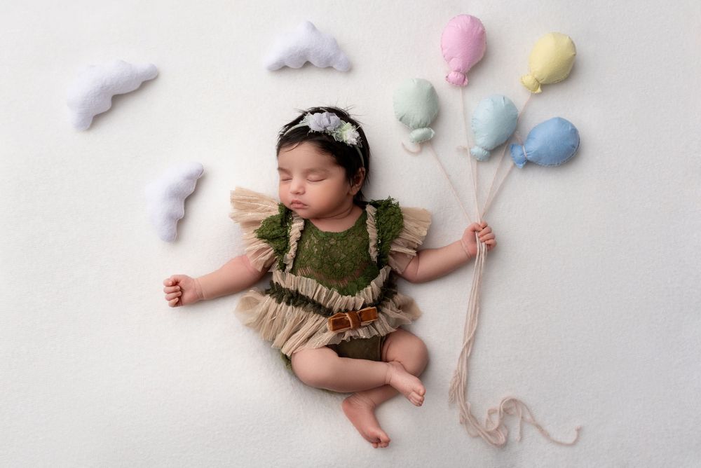 Baby girl in a floral headband holding balloons during a newborn session