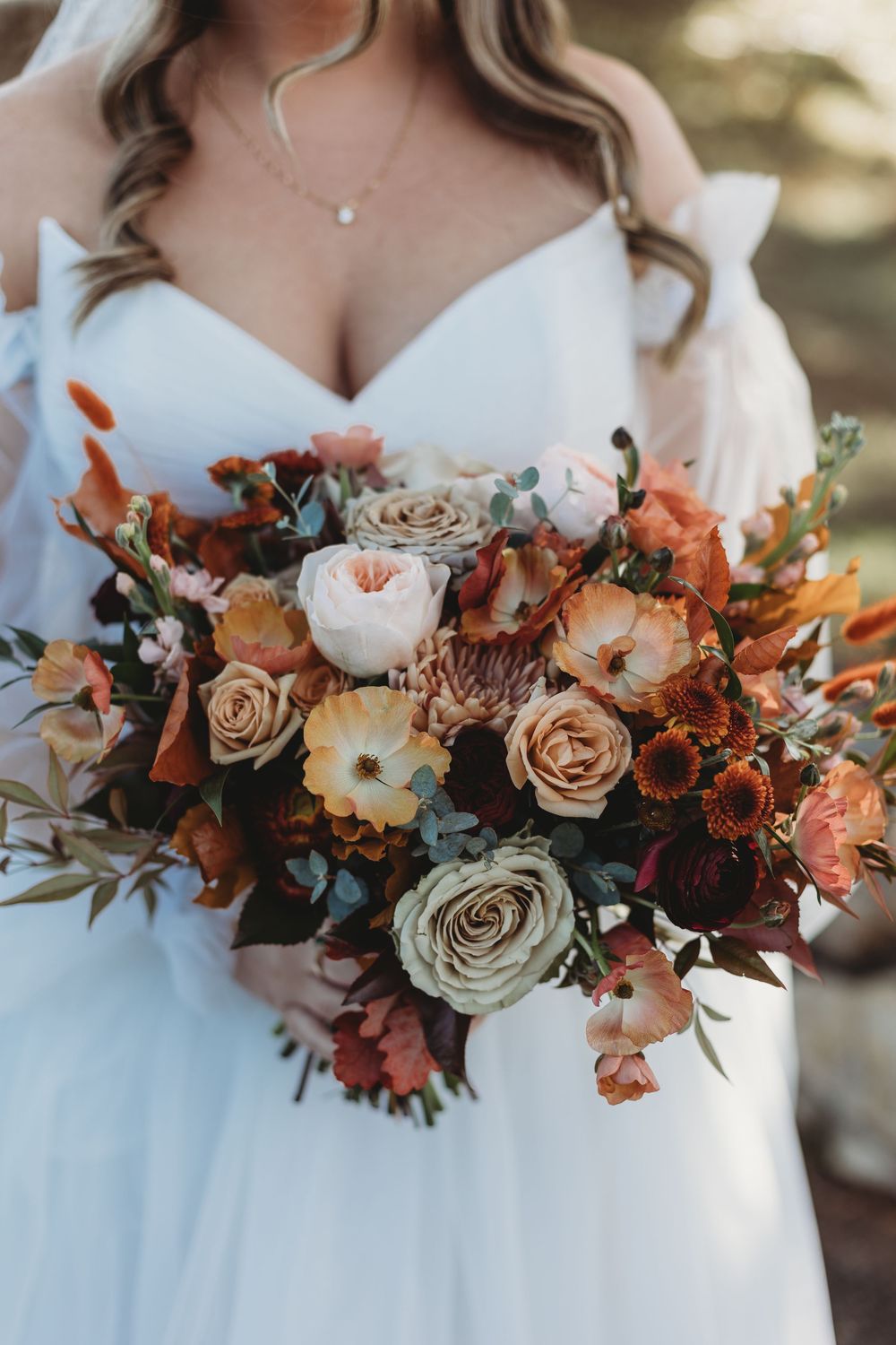 Autumn-toned bridal bouquet with roses and mixed flowers against white wedding dress.