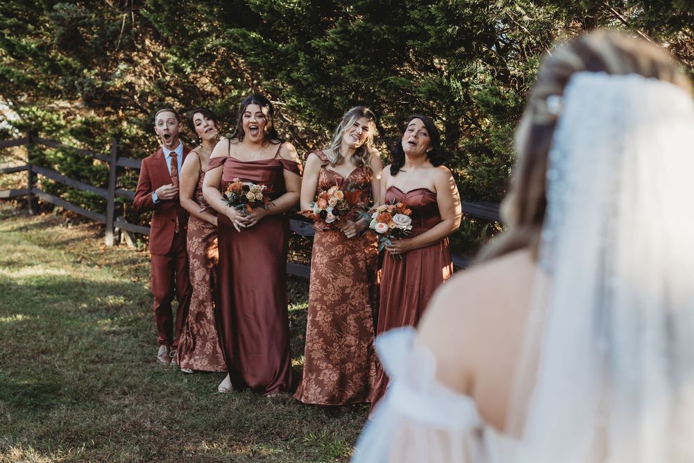 Wedding party in burgundy dresses stands together outdoors during autumn ceremony.