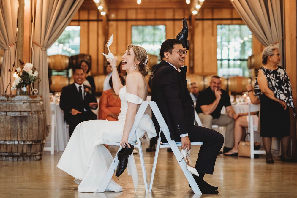 Wedding couple plays fun shoe game during reception in rustic wooden venue.