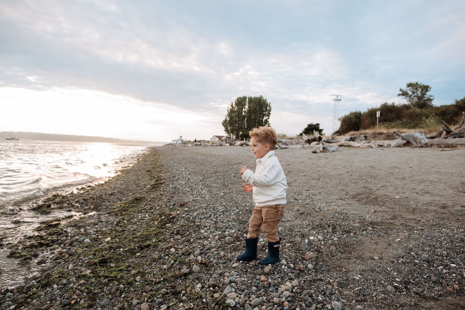 A toddler explores a rocky beach shoreline during golden hour.