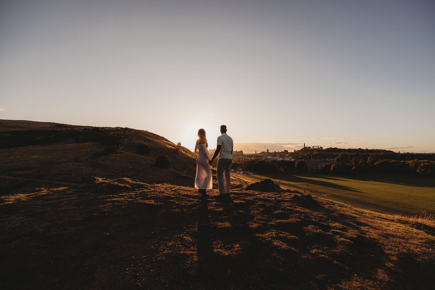 A black and white silhouette of a couple holding hands while walking across a hilltop.