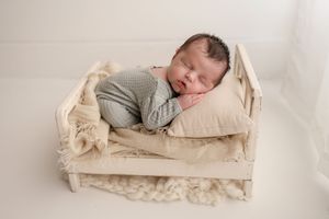 Sleeping newborn baby in gray knit outfit on cream pillow in white wooden mini bed.