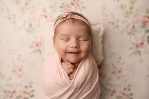 Adorable smiling newborn baby girl swaddled in pink wrap with floral headband.