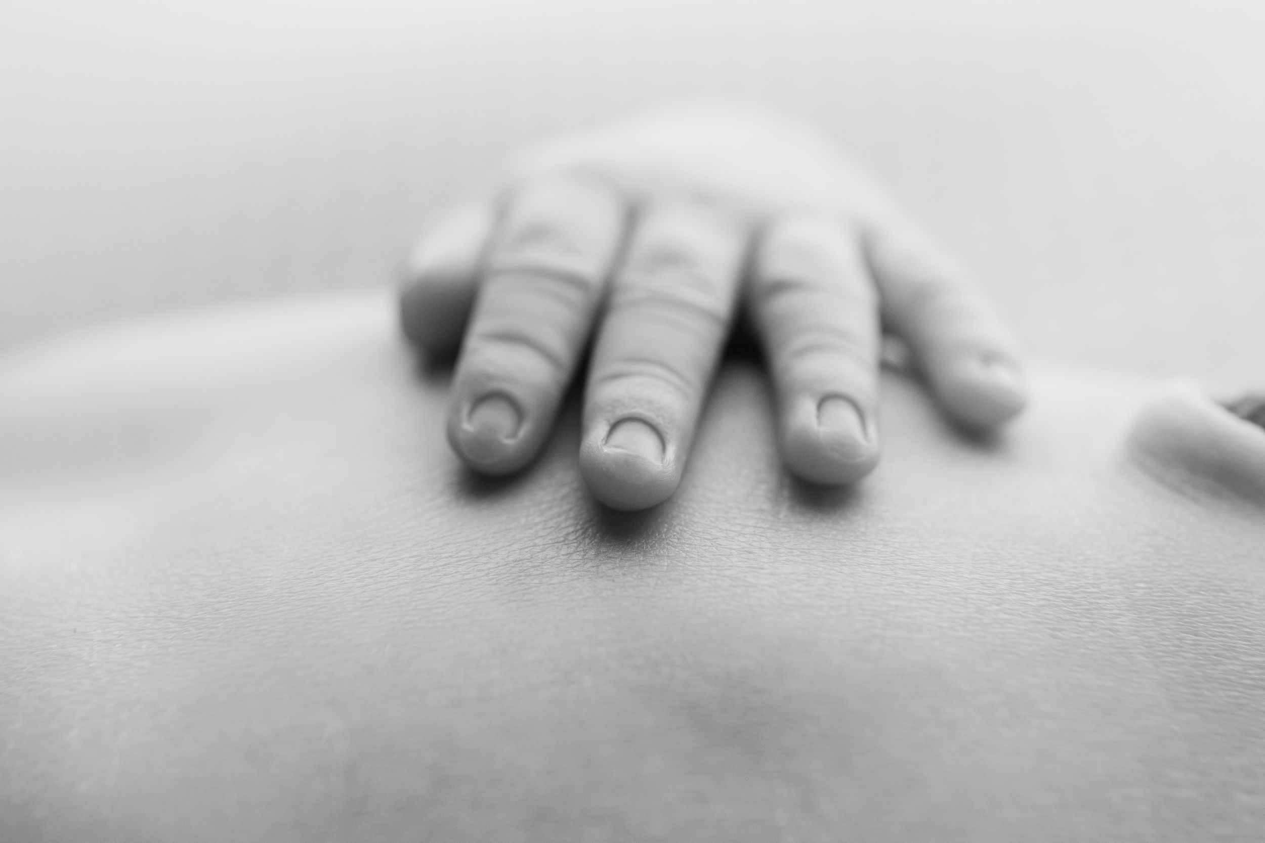 Close-up black and white photo of a parent's hand gently resting on a newborn baby's back.