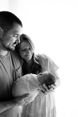 Black and white portrait of parents tenderly holding their sleeping swaddled newborn.