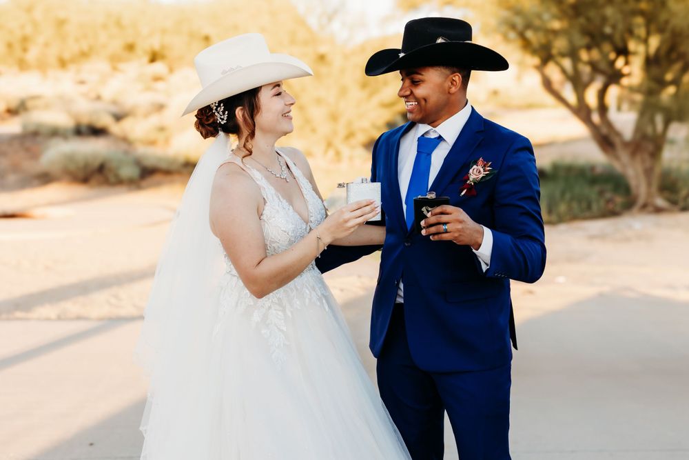 A bride and groom in western attire share drinks at a desert wedding venue.