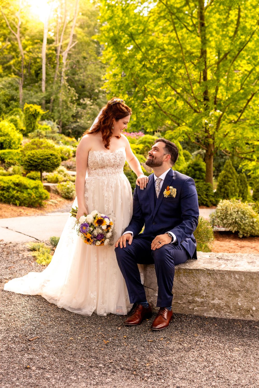 Newlywed couple shares a tender moment in a lush garden setting with golden sunlight filtering through trees.