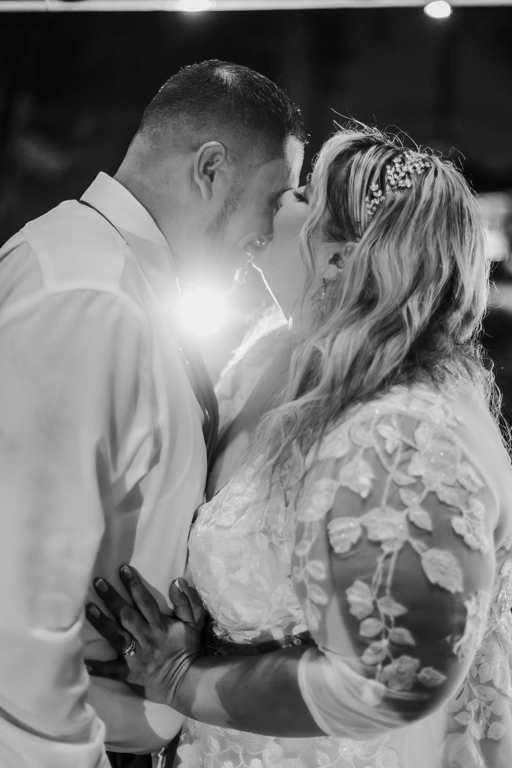A romantic black and white wedding photo showing a tender moment between newlyweds with sunlight glowing behind them.