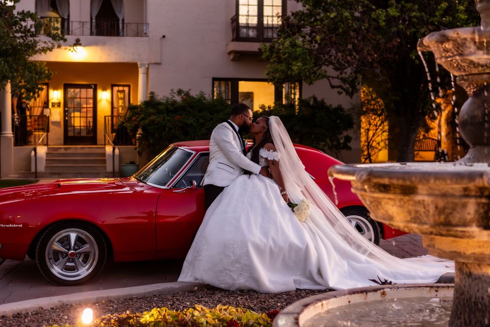 A romantic evening wedding scene with a classic red vintage car parked near an illuminated Mediterranean-style building.