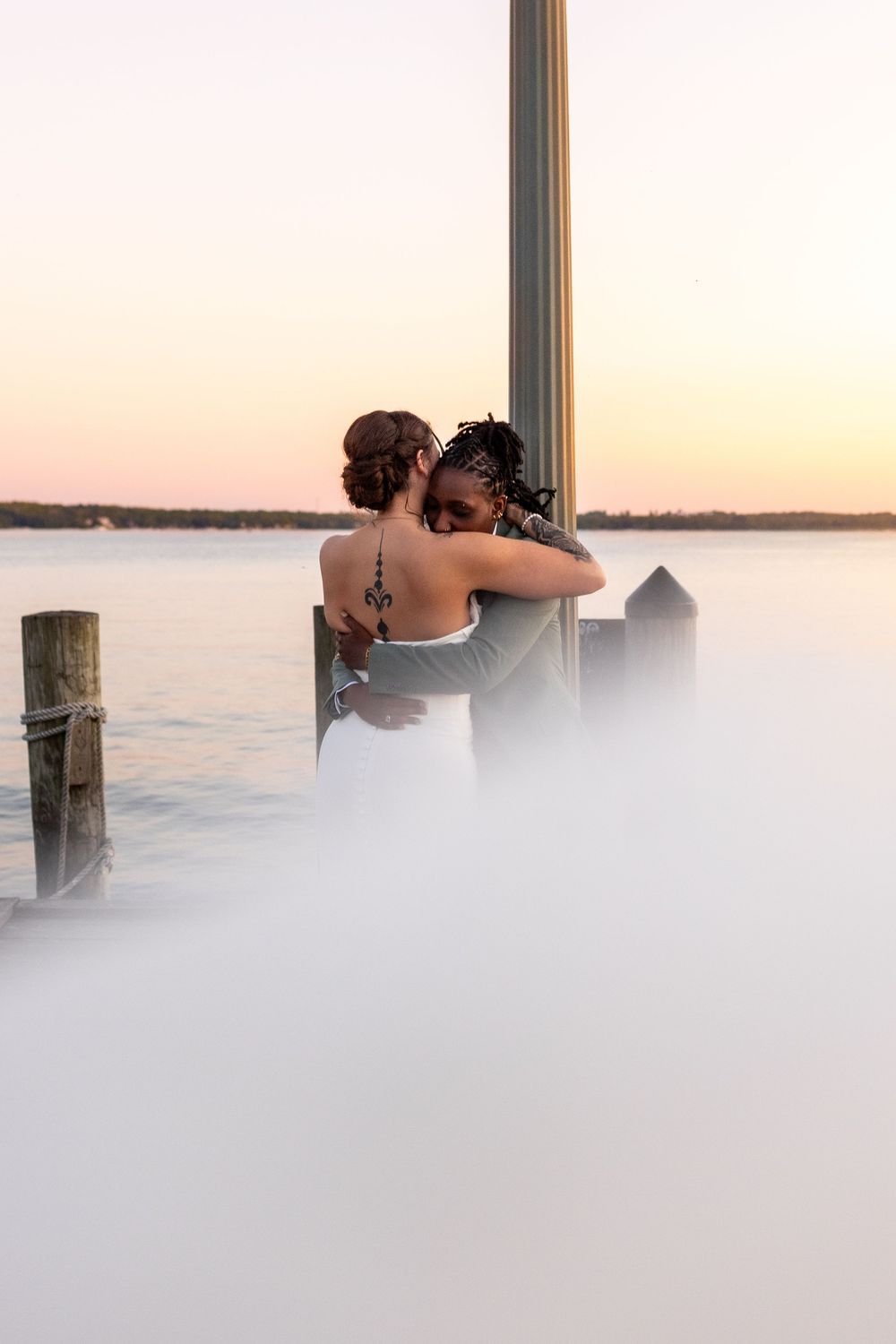 A couple embraces while sitting on a dock overlooking a tranquil lake during a serene sunset.