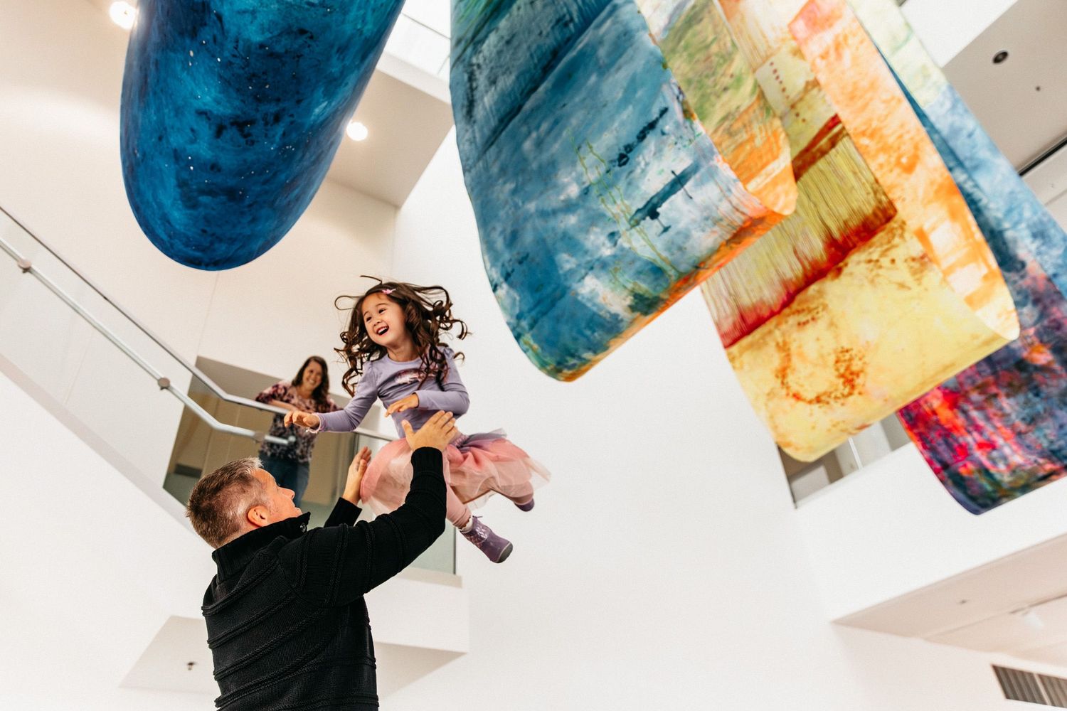 Documentary family photo of a girl being tossed in the air by her dad at a museum in the Twin Cities